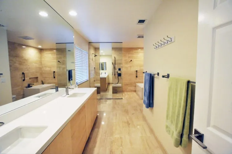 Finished primary bathroom in travertine, with a floating vanity and a glass walk-in shower.