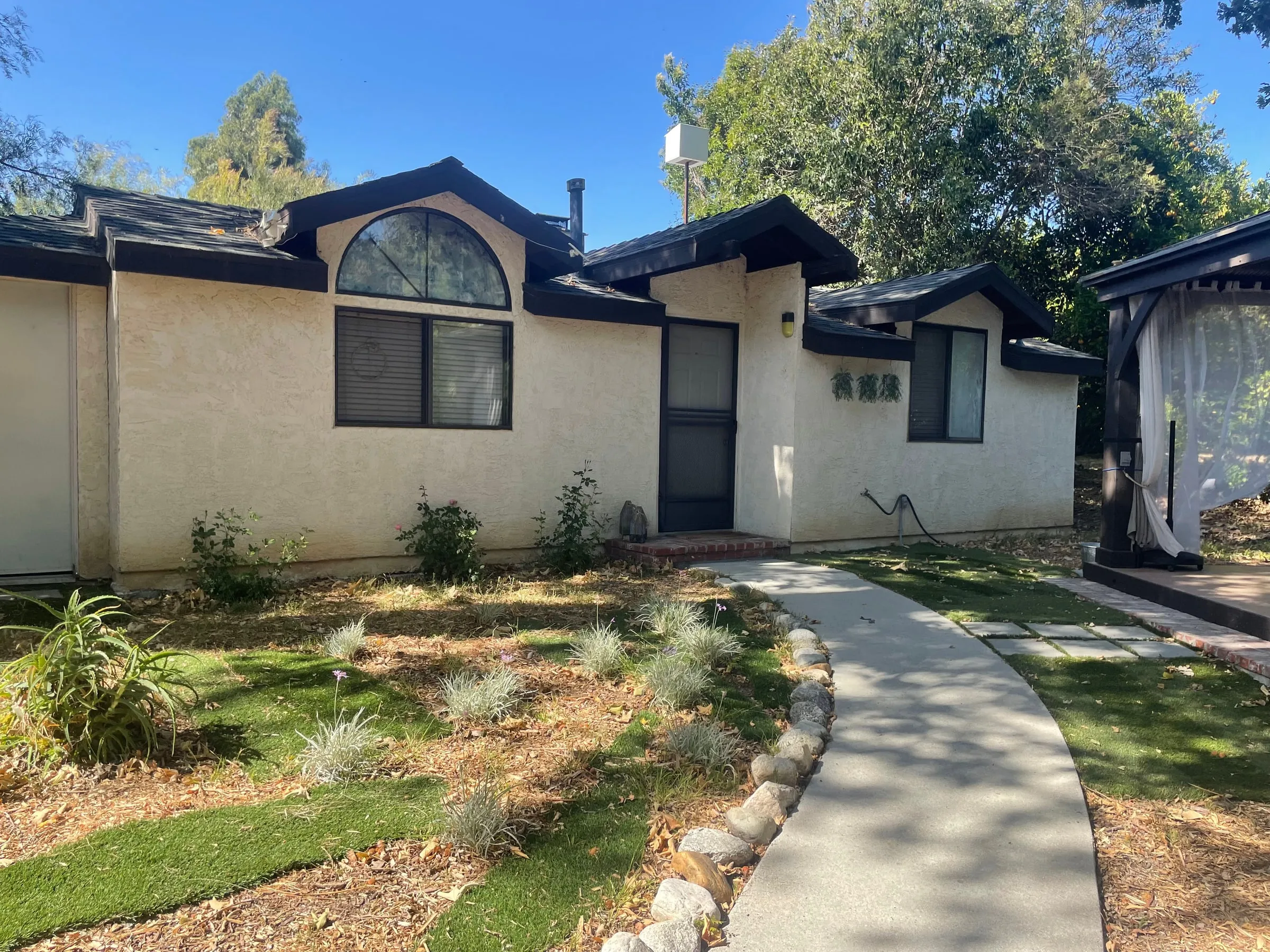 Single-storey stucco home with a dark shingle roof, arched feature window and a covered entry walk.
