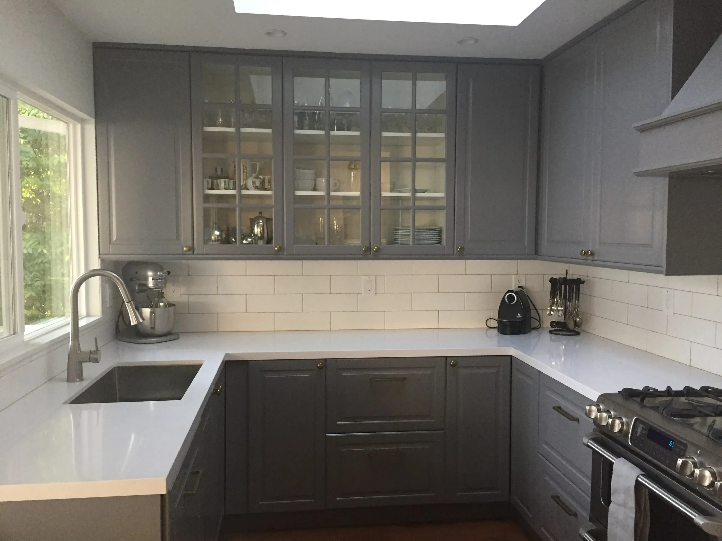 Detail of the finished kitchen: glass-front upper cabinets above a quartz counter and subway tile.