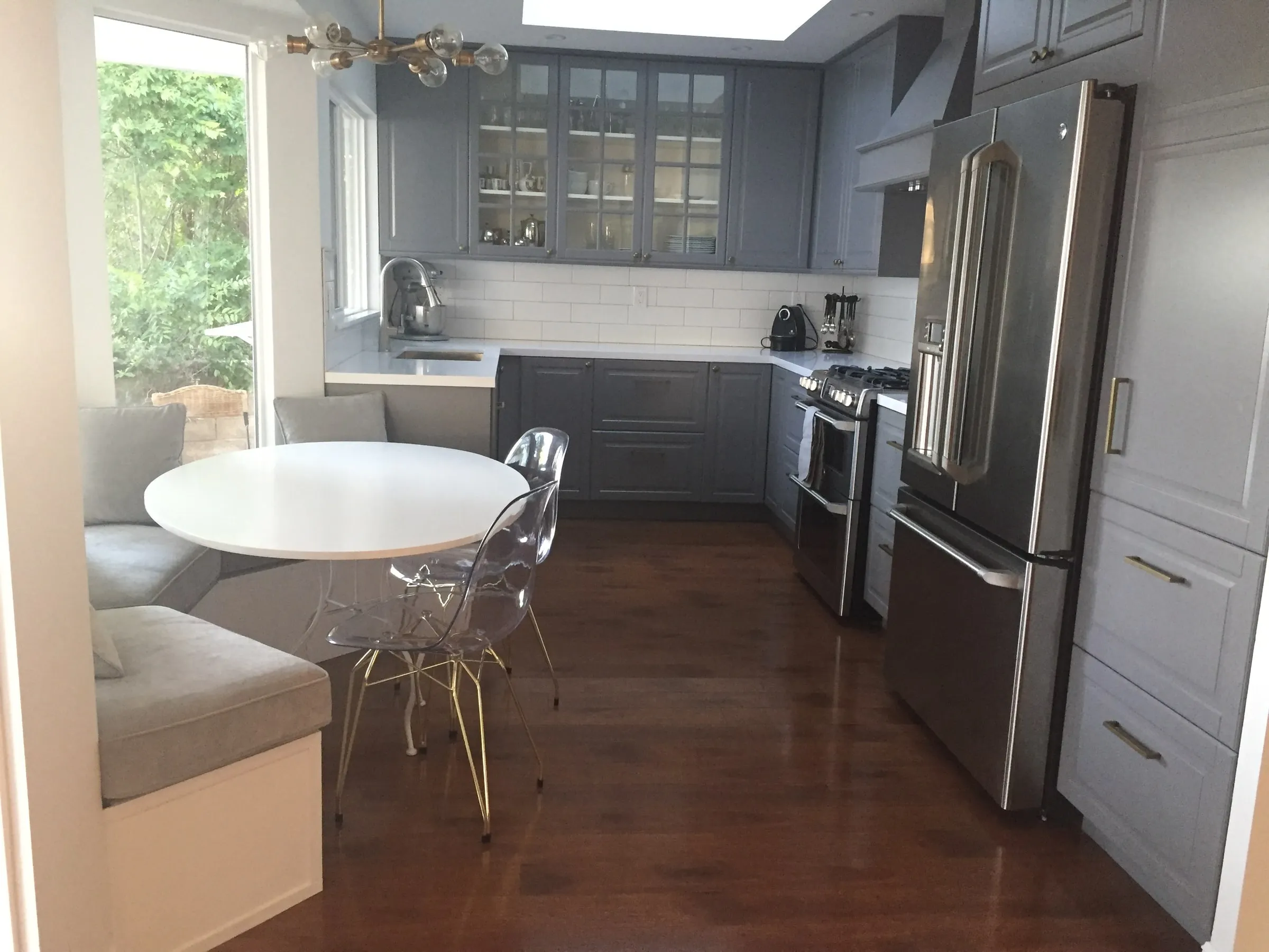 A finished kitchen remodel: grey shaker cabinetry with glass-front uppers, white quartz counters, subway tile to the underside of the cabinets, and a skylight over the run.