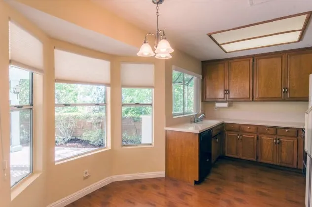 The kitchen before work: oak wall and base cabinets, laminate counters, a fluorescent ceiling box, and a bay window with roller blinds.