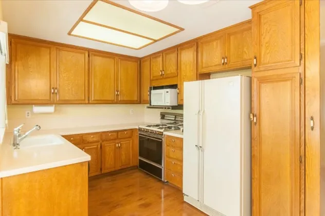 The kitchen before work, from the opposite side: oak cabinets, laminate counters and a dated fluorescent ceiling fixture.